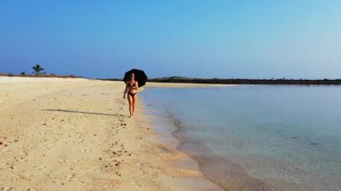 Kumsalda şemsiyeyle yürüyen bikinili seksi kız. Yaz tatili konsepti.  