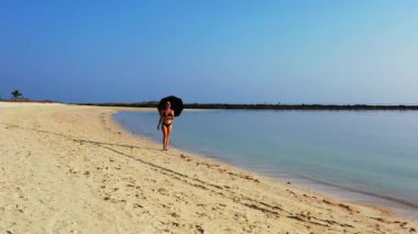 Kumsalda şemsiyeyle yürüyen bikinili seksi kız. Yaz tatili konsepti.  