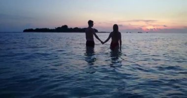 Günbatımında okyanusta duran genç çift