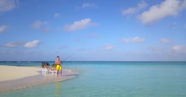 Erkek balık tutarken kız arkadaşı adanın sahilinde dinleniyor. 