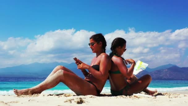 2人の女の子が楽しい時間を過ごし砂浜でパンフレットを読み — ストック動画