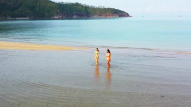Deniz suyunda yürüyen bikinili iki genç kız arkadaş. Tropik tatil köyünde dinlenen güzel kadınlar