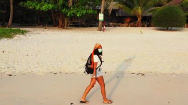 Kumsalda yürüyen maskeli bir kızın görüntüsü. 
