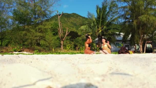 Két fiatal barátnő ül a homokos tengerparton, és beszélgetnek. Gyönyörű nők pihennek trópusi üdülőhelyen 