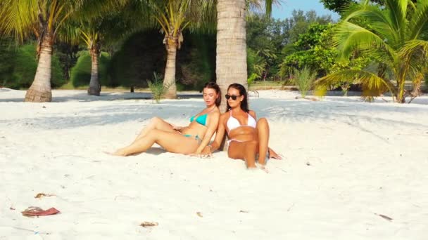 Dwie Młode Dziewczyny Bikini Siedzące Piaszczystym Wybrzeżu Morza Pod Palmą — Wideo stockowe