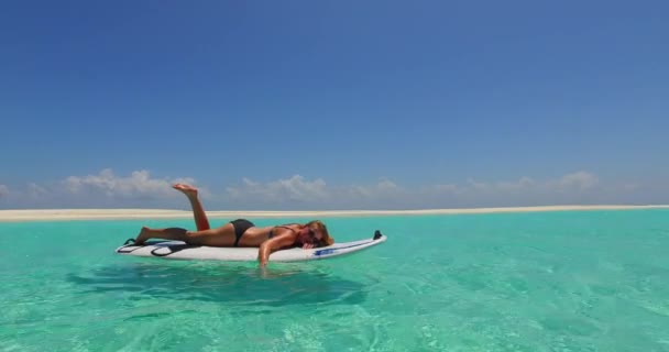 这个晒黑的运动女孩躺在冲浪板上 双手低垂在水里 在波浪中荡秋千的录像 — 图库视频影像