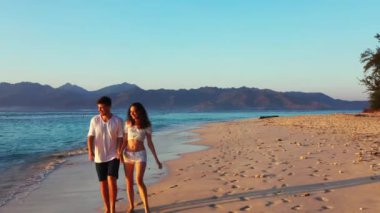 Akşamları kumlu sahilde yürüyen bir çiftin görüntüsü.