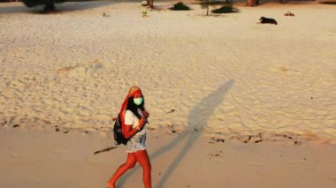 Kumsalda yürüyen maskeli bir kızın görüntüsü. 