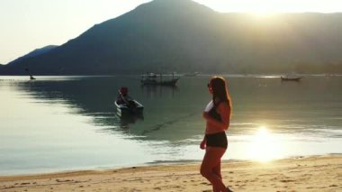 Mayo giymiş çekici genç bir kadın. Güzel adanın okyanusu yakınında dinleniyor, yürüyor ve kulaklıkla müzik dinliyor. 