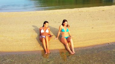 Bikinili iki genç kız deniz kıyısında güneşleniyor. Tropik tatil köyünde dinlenen güzel kadınlar     