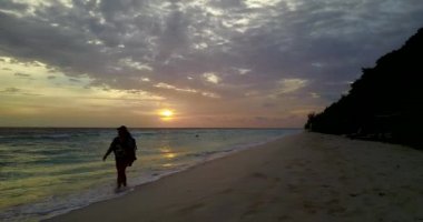 Gün batımında kumsalda yürüyen bir kadın silueti.