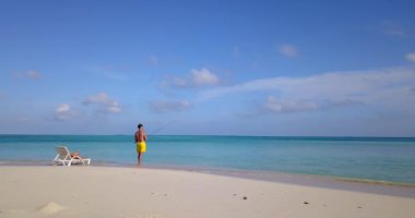 Erkek balık tutarken kız arkadaşı adanın sahilinde dinleniyor. 