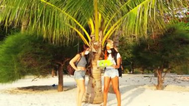 Kumlu sahilde maskeli kızların palmiye ağacının yanında dikilip bir şeyler konuştuklarını ve harita okuduklarını görmek. 