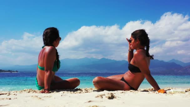 楽しい時間を過ごして砂浜で話をしている2人の女の子は — ストック動画