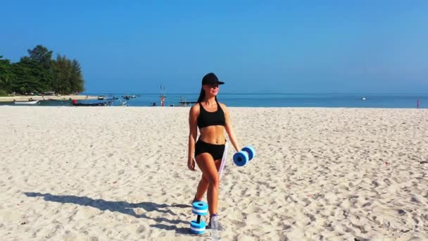 黒水着でブルネット女性行います演習とともにダンベルオンビーチ スポーツコンセプト映像 — ストック動画
