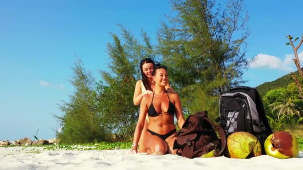 两个年轻的女朋友坐在沙滩上 晒日光浴 一个女孩把防晒霜弄脏了她的女朋友 美丽的女人在热带度假胜地休息 — 图库视频影像