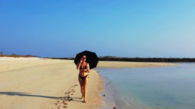 Kumsalda şemsiyeyle yürüyen bikinili seksi kız. Yaz tatili konsepti.  