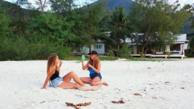Gülümseyen çekici genç bayan arkadaşlar tropik adanın sahilinde tatilin tadını çıkarıyorlar, yaz yolculuğu konsepti görüntüleri. 