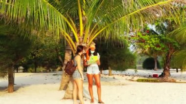 Kumlu sahilde maskeli kızların palmiye ağacının yanında dikilip bir şeyler konuştuklarını ve harita okuduklarını görmek. 