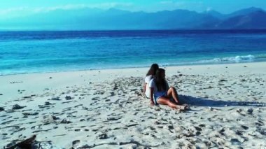 Kızlar kumsalda oturuyor, gündüz vakti.