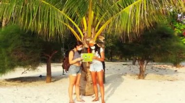 Kumlu sahilde maskeli kızların palmiye ağacının yanında dikilip bir şeyler konuştuklarını ve harita okuduklarını görmek. 