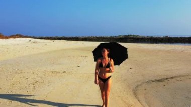 Siyah bikinili genç çekici kız kumlu sahilde yürüyor, yaz tatili konsepti  