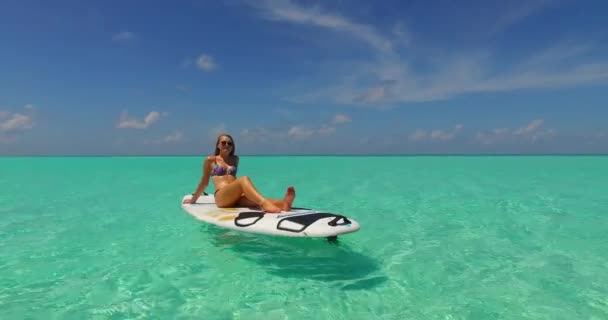 サーフボードで日光浴をして波に揺れる運動女子の映像です — ストック動画