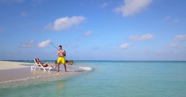 Homem Pesca Enquanto Sua Namorada Relaxando Perto Praia Ilha — Vídeo de Stock