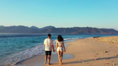 Tropikal sahilde yürüyen ve tatilin tadını çıkaran genç bir çift. Yaz tatili konsept videosu. Aşık bir adam ve bir kadın dışarıda dinleniyor. 