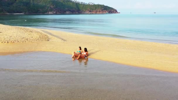 Két fiatal bikinis barátnő fekszik a tengerparton. Gyönyörű nők pihennek trópusi üdülőhelyen     