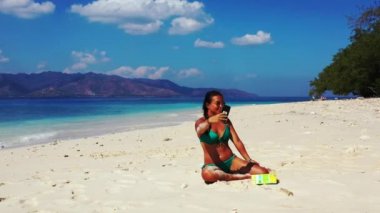 Tropik plajda akıllı telefon kullanan güzel genç bir kadın.