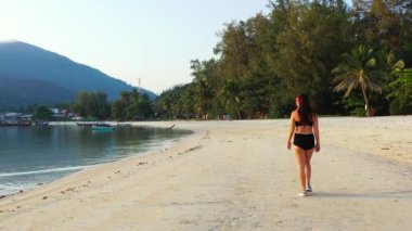 Sahilde yürüyen kulaklıklı bir kadın ve soğuk yaz gezisi konsepti. 