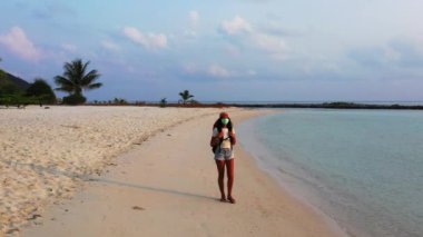 Kumsalda yürüyen maskeli bir kızın görüntüsü. 