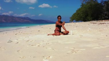 Tropik plajda akıllı telefon kullanan güzel genç bir kadın.