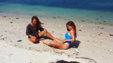 İki kızın kumsalda oturup birbirleriyle konuşarak güzel vakit geçirmesini izlemek.