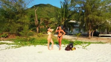 Kumlu deniz kıyısında güneşlenen ve konuşan iki genç kız arkadaş. Tropik tatil köyünde dinlenen güzel kadınlar    