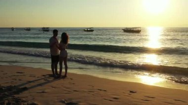 Okyanus ve tropikal sahilde dramatik bir gün batımı. Kıyı şeridinde duran genç çift, seyahat kavramı 