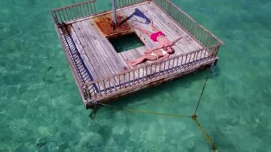 Genç adam ve kadın deniz suyunda tahta duba üzerinde yüzüyorlar. Tropik bir tatil köyünde dinlenen güzel bir çift. 