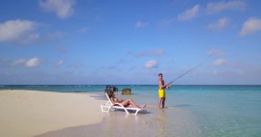 Erkek balık tutarken kız arkadaşı adanın sahilinde dinleniyor. 