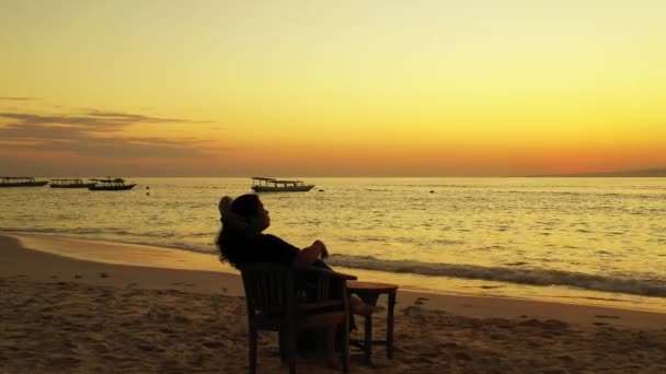 日落时快乐的女人坐在沙滩上的椅子上 — 图库视频影像