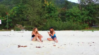 Gülümseyen çekici genç bayan arkadaşlar tropik adanın sahilinde tatilin tadını çıkarıyorlar, yaz yolculuğu konsepti görüntüleri. 