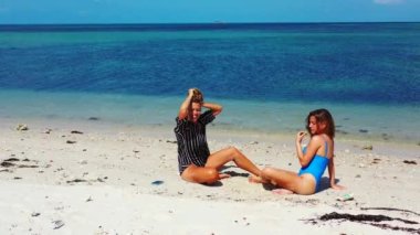 İki kız kumsalda güzel vakit geçiriyorlar. Oturuyorlar ve birbirleriyle konuşuyorlar.
