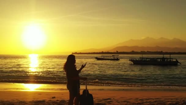 Σιλουέτα Της Γυναίκας Στέκεται Βαλίτσα Στην Παραλία Και Χρήση Smartphone — Αρχείο Βίντεο