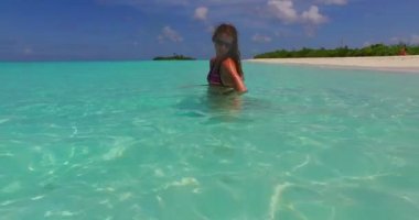 Bikini giyen kıvırcık kadın Maldivler 'de ferahlatıcı suyla cildini nemlendiriyor.