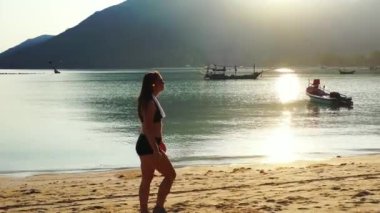 Mayo giymiş çekici genç bir kadın. Güzel adanın okyanusu yakınında dinleniyor, yürüyor ve kulaklıkla müzik dinliyor. 