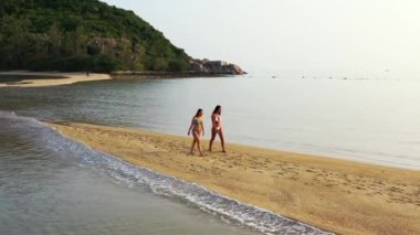 Deniz kıyısında yürüyen bikinili iki genç kız arkadaş. Tropik tatil köyünde dinlenen güzel kadınlar      