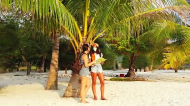 Kumlu sahilde maskeli kızların palmiye ağacının yanında dikilip bir şeyler konuştuklarını ve harita okuduklarını görmek. 