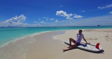 Okyanus kıyısındaki SUP küreğinde oturan genç adam.