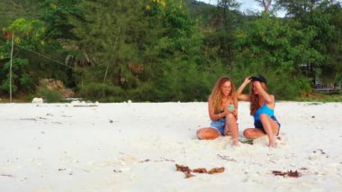 Gülümseyen çekici genç bayan arkadaşlar tropik adanın sahilinde tatilin tadını çıkarıyorlar, yaz yolculuğu konsepti görüntüleri. 