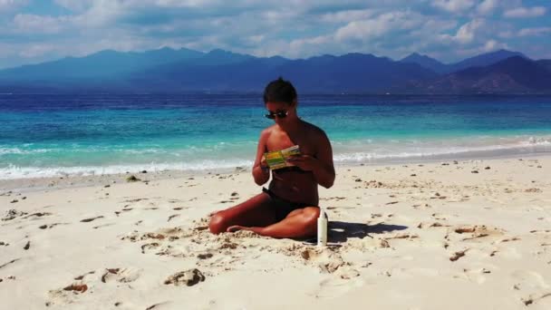 美しい若い女性が熱帯のビーチで雑誌を読んで — ストック動画